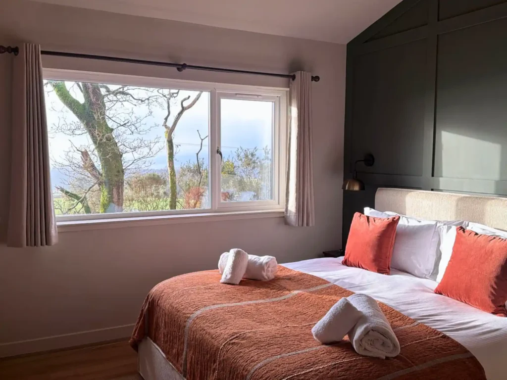 Master bedroom at Millers Hill lodge with king-size bed, green panelled wall and woodland views